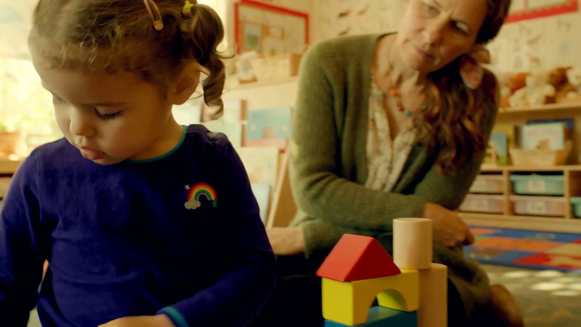 A student's hand resting beside a young plant and wooden puzzle blocks on a classroom desk